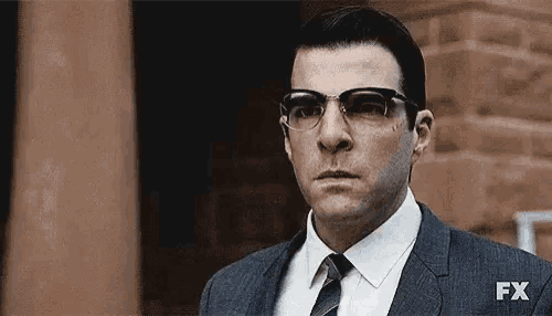 a man in a suit and tie is wearing glasses and looking at the camera .