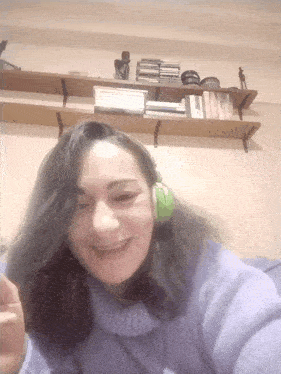 a woman wearing green headphones smiles in front of a bookshelf