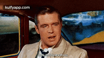 a man in a suit and tie is sitting in a car talking to holly .