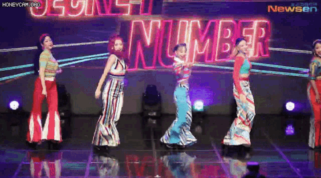 a group of young women are dancing on a stage in front of a neon sign that says number .