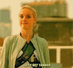 a woman in a green jacket says let 's get tanked in front of a building
