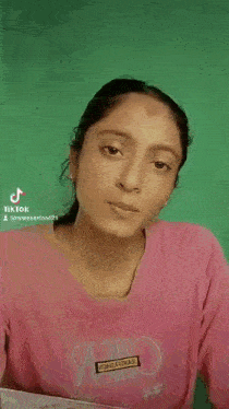 a woman in a pink shirt is making a funny face while holding something to her face .