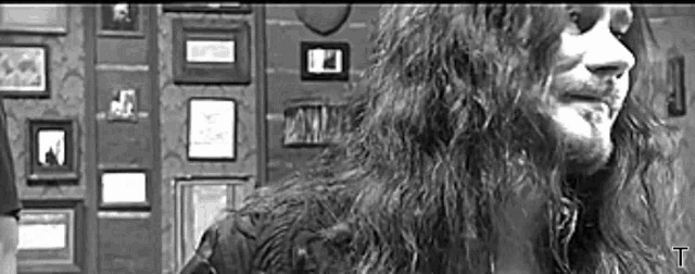 a man with long hair is standing in front of a wall with pictures on it