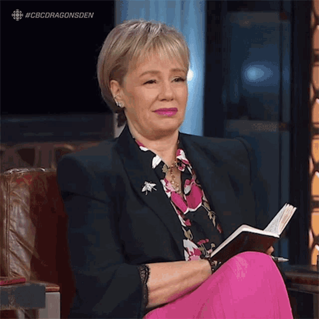 a woman is sitting in a chair reading a book with the hashtag #cbcdragonsden on the bottom