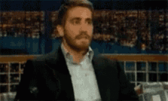 a man in a suit and tie is making a surprised face while sitting in front of a crowd .