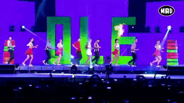 a group of people dancing on a stage with a mad logo