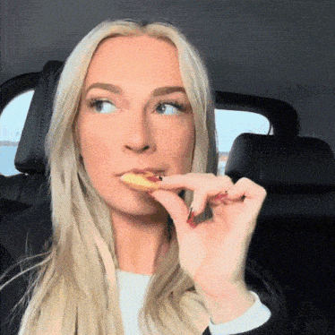 a blonde woman with red nails is eating a french fry