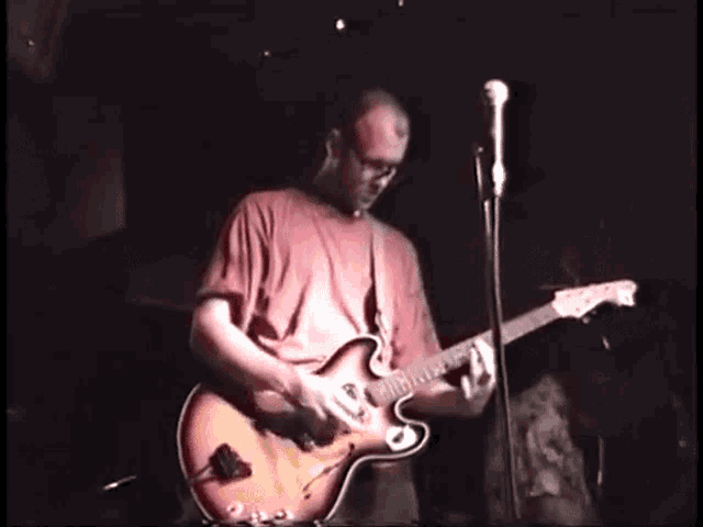 a man playing a guitar in front of a microphone in a dark room