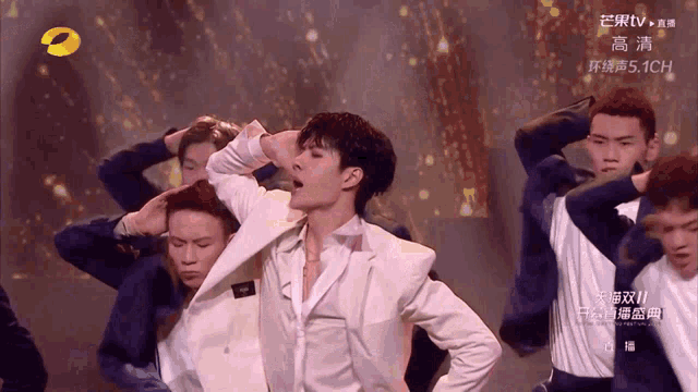a man in a white suit stands in front of a group of dancers on a tv screen