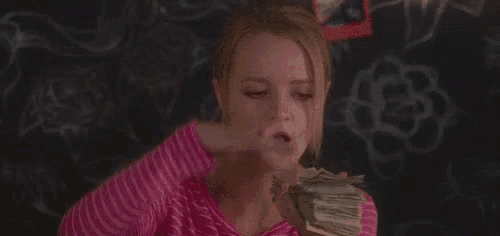 a woman is blowing money in the air while holding a stack of money in her hand .