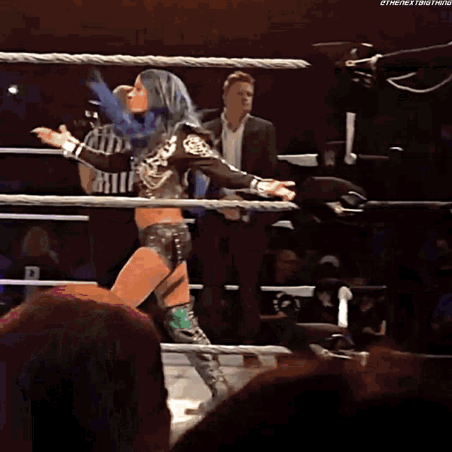 a woman with blue hair is standing in a wrestling ring while a referee watches