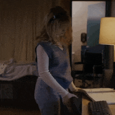 a woman in a blue vest is standing in front of a desk with a keyboard