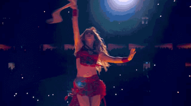 a woman in a red dress is dancing on a stage with her arms outstretched