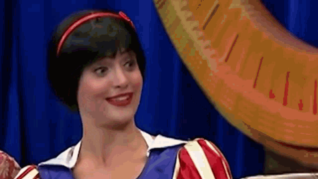 a woman in a snow white costume is smiling in front of a large banana .