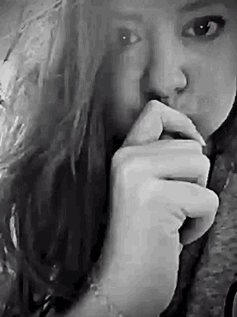 a black and white photo of a girl covering her mouth with her hand .