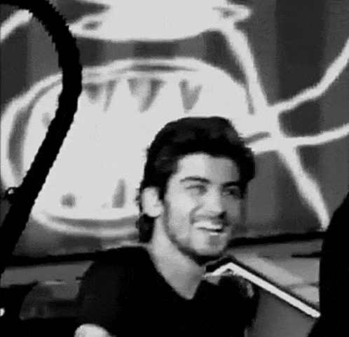 a black and white photo of a man with a beard smiling in front of a clock .