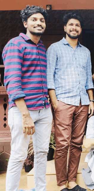 two men standing next to each other with their hands in their pockets and smiling