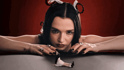 a woman with black nails is laying on a table with a doll in her hands