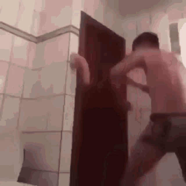 a shirtless man is standing in a bathroom holding a door open .