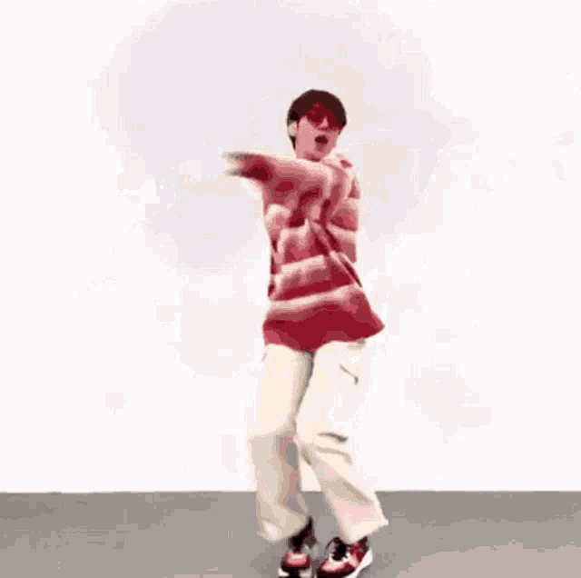 a man wearing a red and white striped sweater and white pants is dancing in front of a white wall .