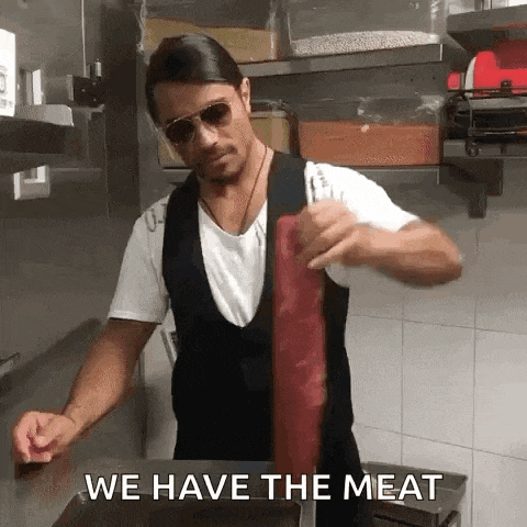 a man wearing sunglasses is holding a piece of meat in a kitchen .