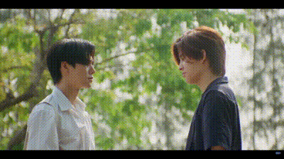 two young men are standing next to each other and looking at each other in front of a tree .