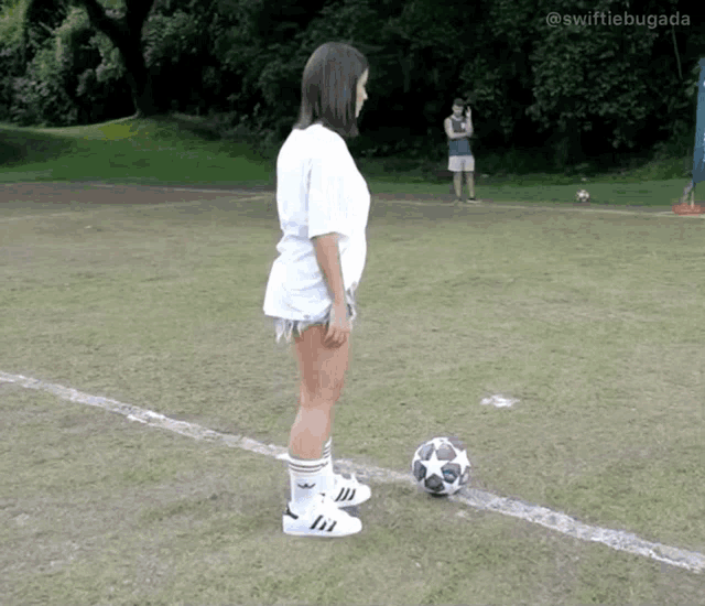 a woman standing next to a soccer ball on a field with swiftiebugada written on the bottom right