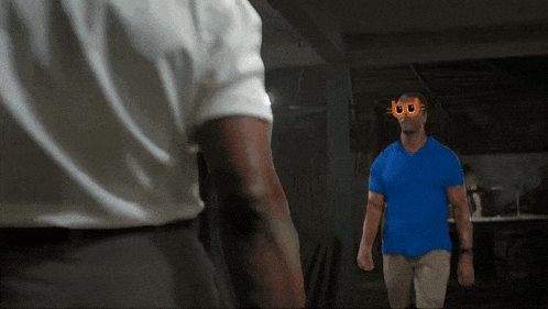 a man in a blue shirt with a mask on his face stands in front of another man in a white shirt