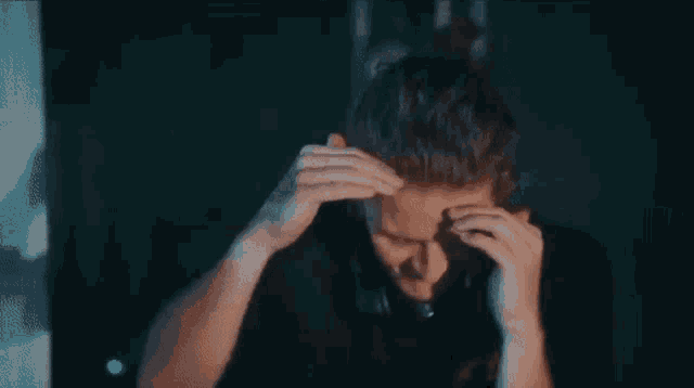 a man is covering his face with his hands while sitting in front of a computer screen .