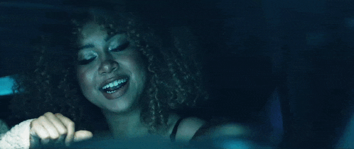 a woman with curly hair is sitting in a car at night and smiling .