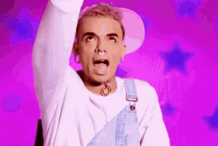 a man wearing overalls and a pink hat is standing in front of a purple background .