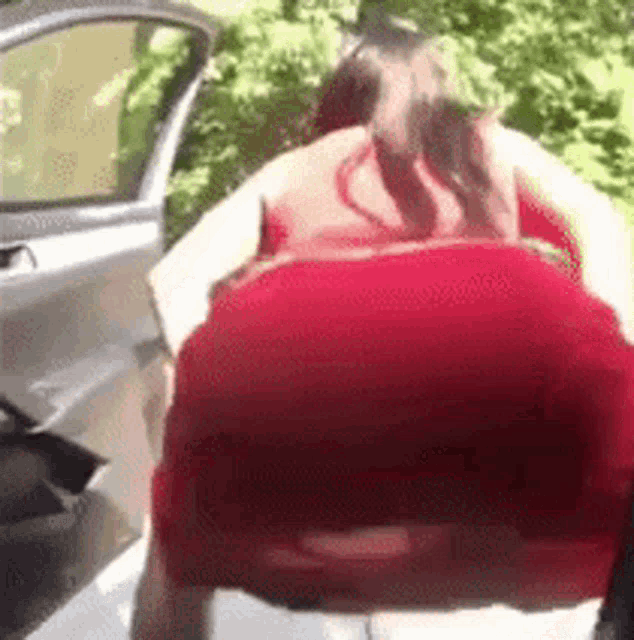 a woman in a red dress is standing next to a car with her back to the camera .