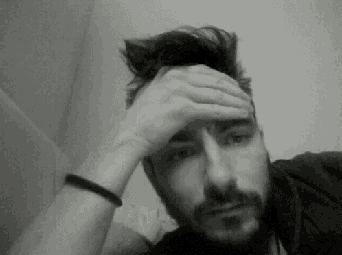 a man with a beard holds his hand to his forehead in a black and white photo