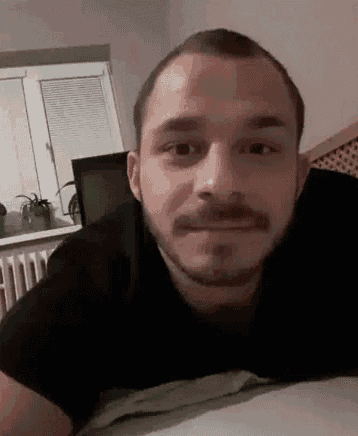a man with a beard and mustache is laying on a bed and smiling at the camera .