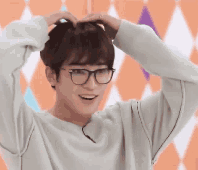 a young man wearing glasses and a sweater is making a heart shape with his hands on his head .
