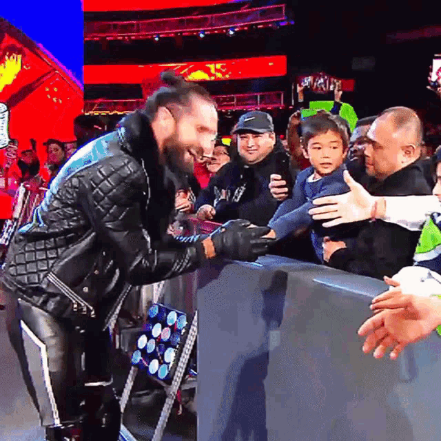 a man in a leather jacket is shaking hands with a child