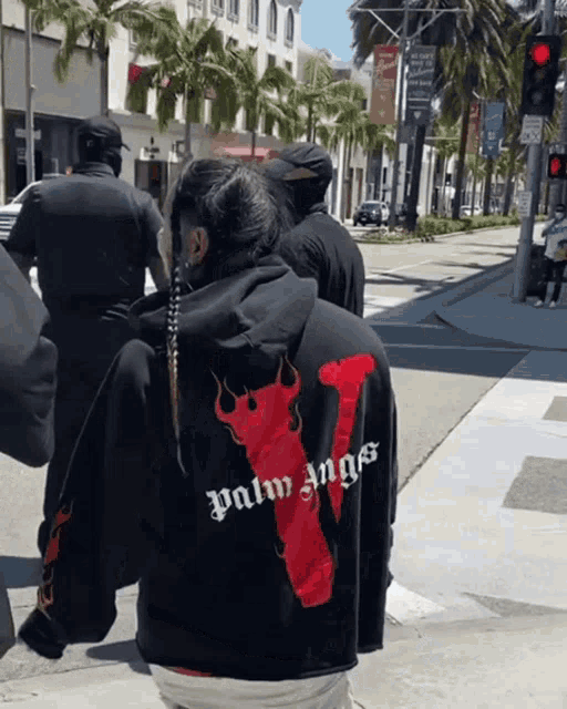 a person wearing a black palm angels hoodie is walking down the street