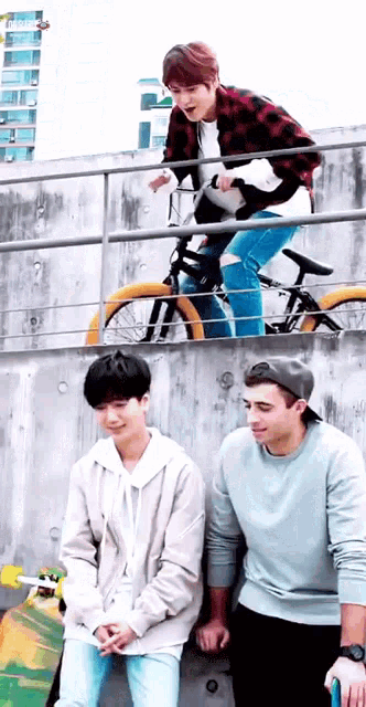 a man is riding a bike while two other men sit on skateboards .