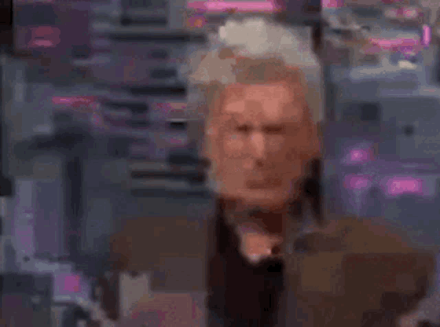 a man in a suit and black shirt is making a funny face while sitting on a stage .