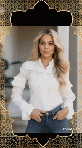 a woman wearing a white ruffled shirt and blue jeans stands in front of a black and gold frame
