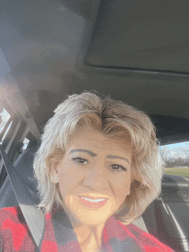 a woman in a red and black plaid shirt is smiling in a car