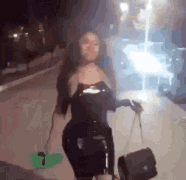 a woman in a black dress is walking down a street holding a purse