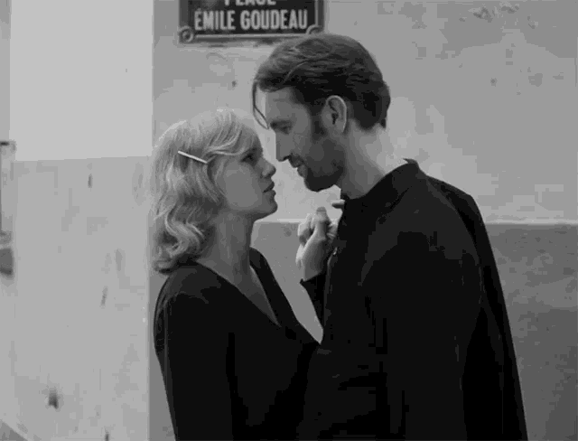a man and woman are kissing in front of a sign that says emile goudau