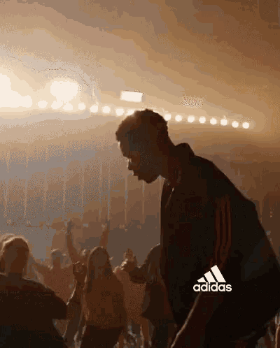 a man is dancing in front of a crowd with the adidas logo in the background .