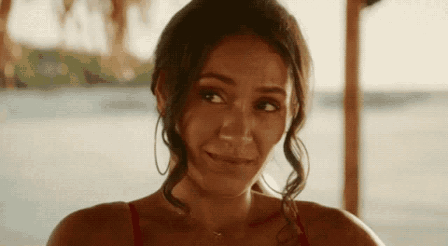 a woman in a red bikini is smiling and looking at the camera while sitting on a beach .
