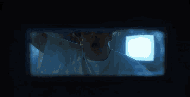 a man in a white shirt is looking through a hole in a window .
