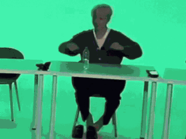 a man is sitting at a table with his legs crossed and a bottle of water on it .