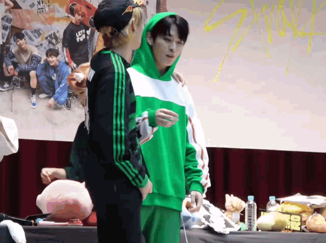 a man in a green hoodie stands next to a man in a black hat