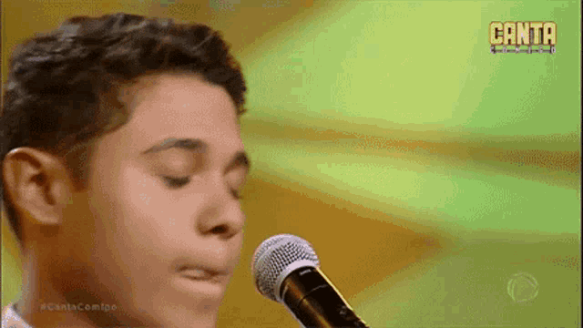 a young man singing into a microphone with canta written on the screen behind him