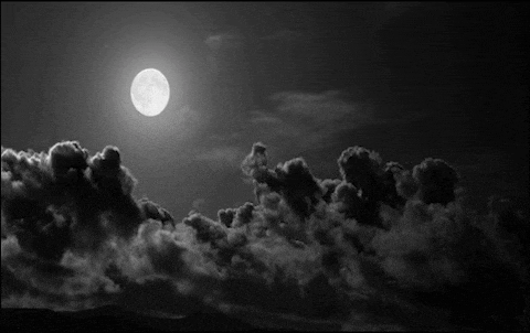 a black and white photo of a full moon in a cloudy night sky